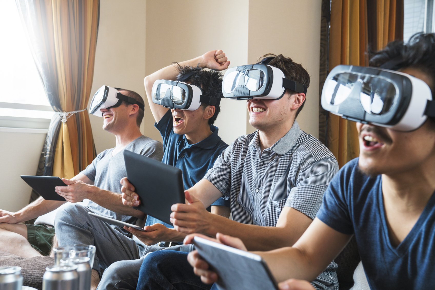 Group of friends sat on the sofa playing games using virtual reality headsets and digital tablets as controllers. Kyoto, Japan. May 2016