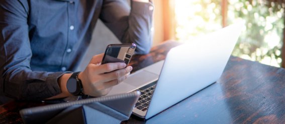 Male hand holding smartphone. Businessman using laptop computer and digital tablet while working in the cafe. Mobile app or internet of things concepts. Modern lifestyle in digital age. (Male hand holding smartphone. Businessman using laptop computer