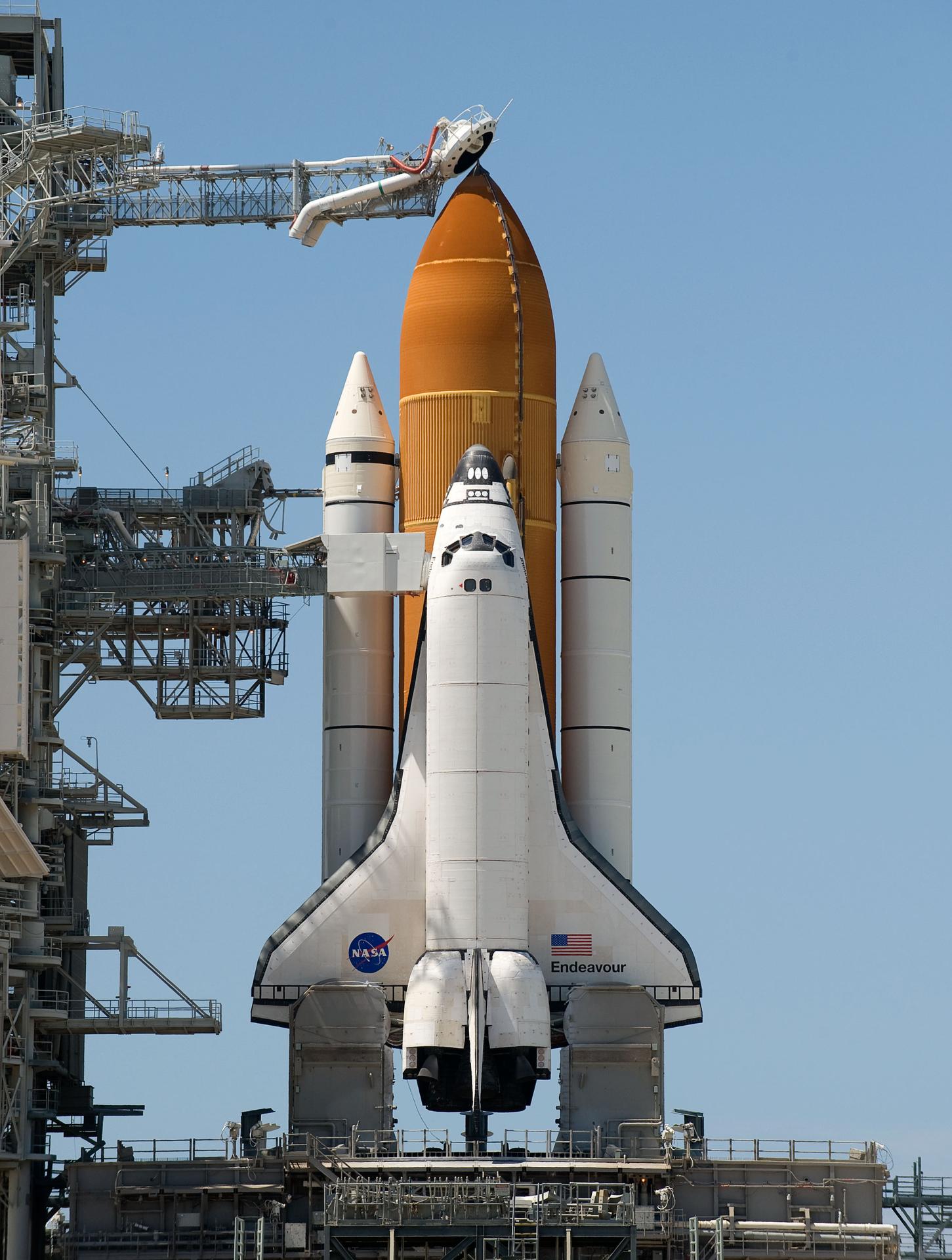 กระสวยอวกาศ Endeavour ที่ฐานปล่อย ซึ่งจะถูกวางตั้งยึดติดกับแทงค์ด้านนอก (สีส้ม) และจรวดผลักดัน (สีขาวขนาบข้าง)