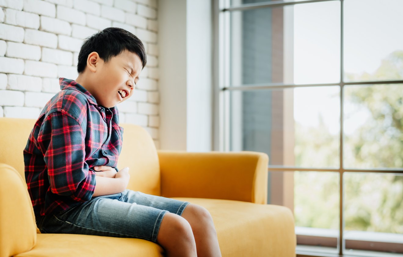 A little Asian boy has a stomachache. Holding his belly with both hands and suffering on sofa