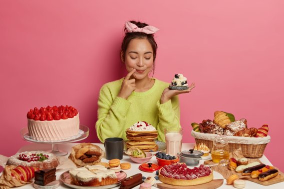 Pleased brunette woman holds small creamy muffin, bakes many desserts for New Year holiday or festive time, demonstrates her culinary abilities, has special occasion, degustates homemade cupcake