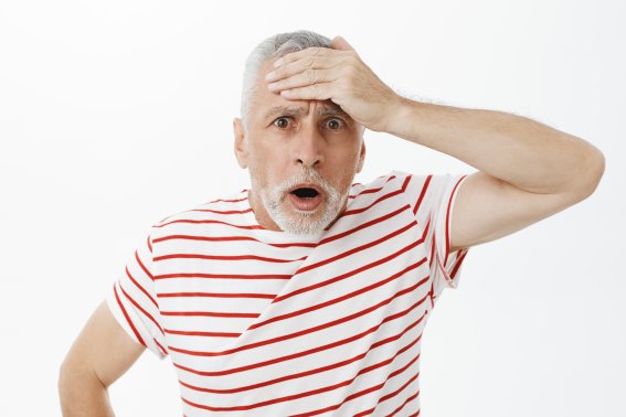 Portrait of shocked speechless concerned old man punching forehead with palm with troubled look open mouth and looking at camera troubled having terrible problem posing disturbed over grey wall.